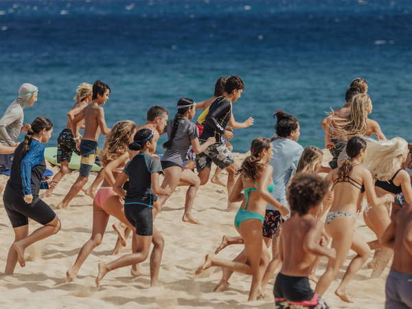 A group of kids running towards the ocean at the North Shore Junior Lifeguard program