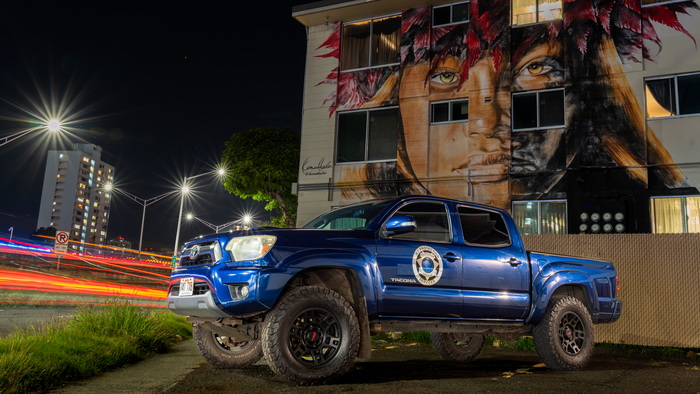 KT Protection Services truck at night in front of a building with a giant painting of person on it.