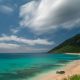 An uncrowded beach in Hawaii with green water, blue sky, and white clouds
